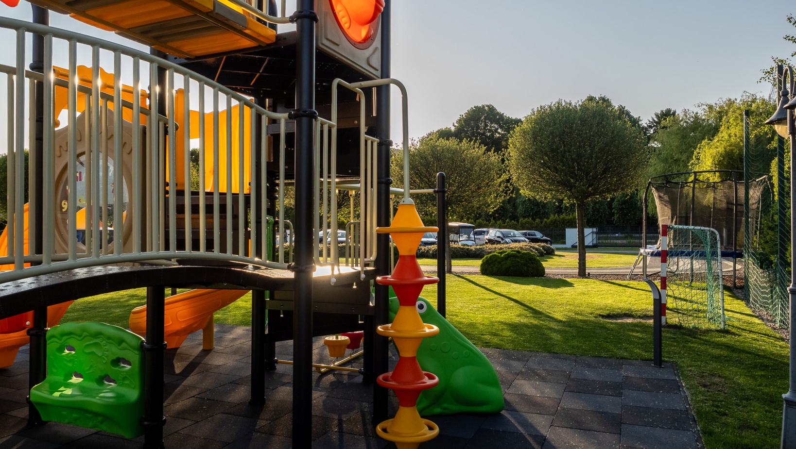 Kolorowy plac zabaw na zewnątrz zjeżdżalniami, bezpieczną gumową nawierzchnią, trampoliną i bramką na słonecznym trawniku.