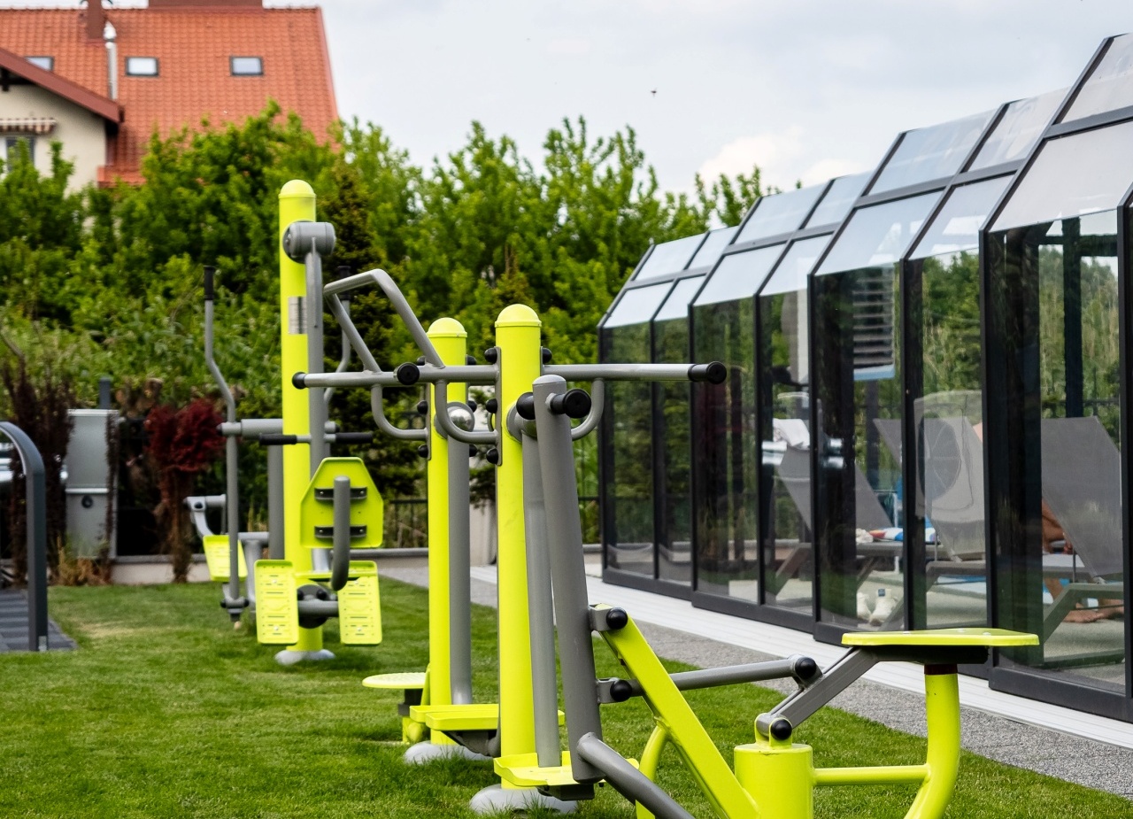 Outdoor fitness stations on a manicured lawn beside a glass-enclosed pool with sun loungers and garden views.
