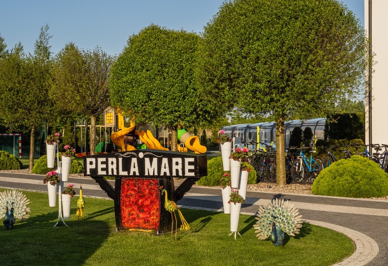 PERLA MARE sign on manicured lawn with decorative peacocks, flowering planters, children's slides and a row of guest bicycles.