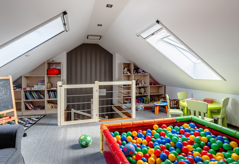 Bright attic children's playroom with ball pit, skylights, small table and chairs, toy shelves and chalkboard