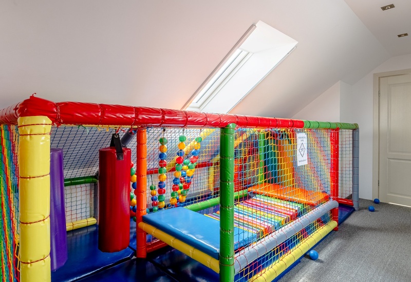 Colorful indoor soft-play enclosure under a skylight with padded obstacles, ball area and seating — children's playroom