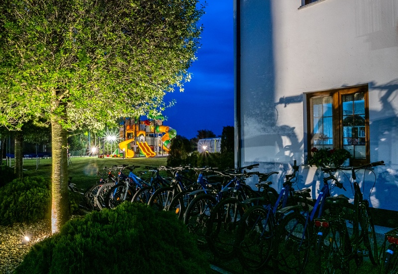Night hotel grounds with guest bicycles by the building, a lit tree and a colorful children's playground visible