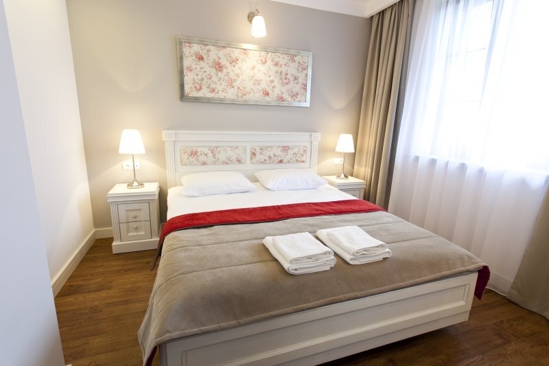 Bright, cozy double hotel room with floral headboard, bedside lamps, red bed runner and folded towels.