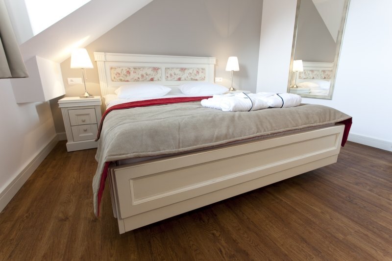 Cozy attic double room with queen bed, floral headboard, bedside lamps, wooden floor and folded bathrobes on soft neutral bedding