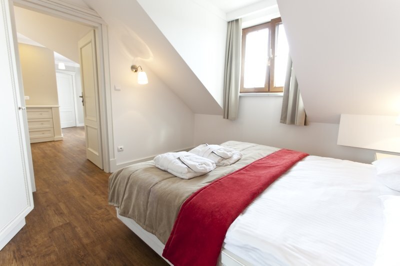 Attic double room with sloped ceiling, wooden floor, double bed with red runner and bathrobes, soft lamps