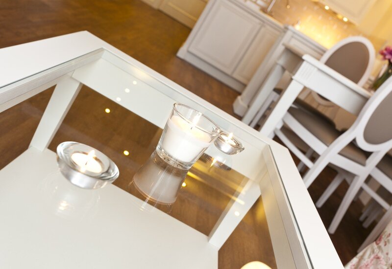 Three lit glass candles on a glass-top white coffee table in a bright dining/lounge with white chairs