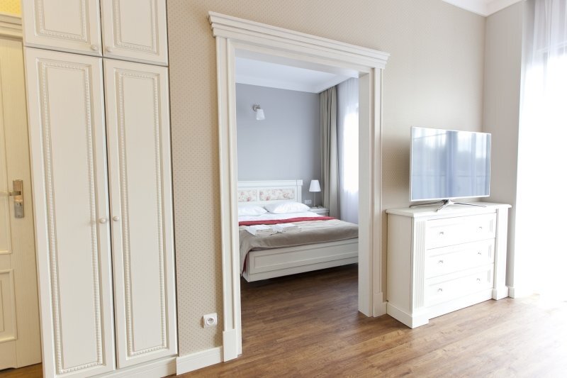 Bright classic suite with hardwood floors, built-in wardrobe, TV on dresser and separate bedroom with queen bed and bedside lamp