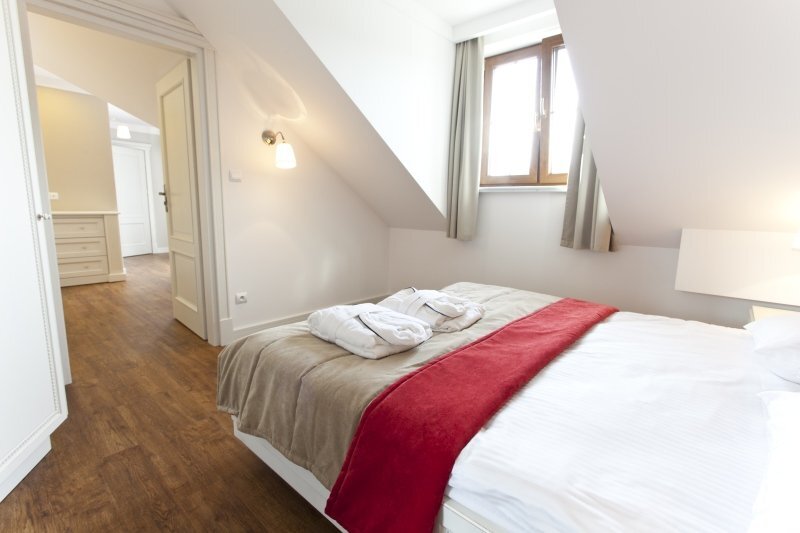 Attic double room with sloped ceiling, large bed with red runner, plush robes on bed, wooden floor and soft natural light