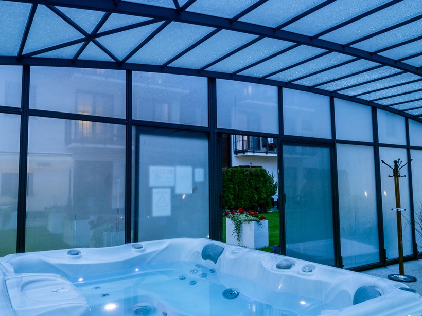 Enclosed glass atrium with illuminated hot tub, wicker seating, coat stand and garden view