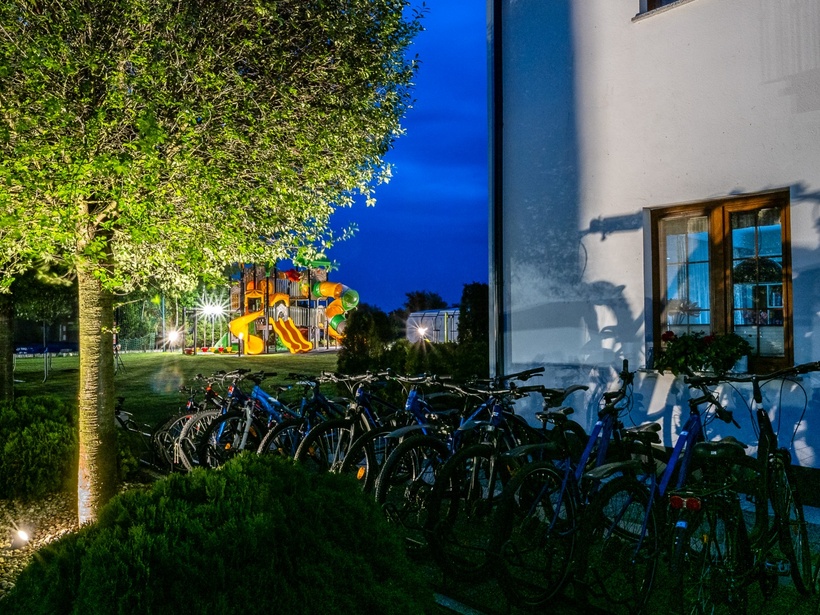Night hotel grounds with guest bicycles by the building, a lit tree and a colorful children's playground visible