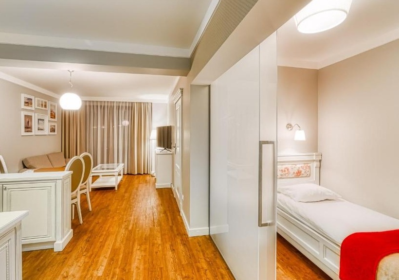 Studio z jednoosobowym łóżkiem za przesuwną szklaną ścianką, salon z sofą, stołem, telewizorem i drewnianą podłogą