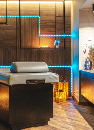 Moderner Spa-Raum mit komfortabler Massageliege, stimmungsvoller Beleuchtung und warmen Holzakzenten
