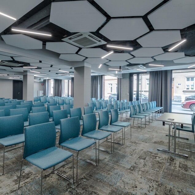Modern hotel conference room with blue chairs, geometric ceiling panels, and large windows overlooking the street.