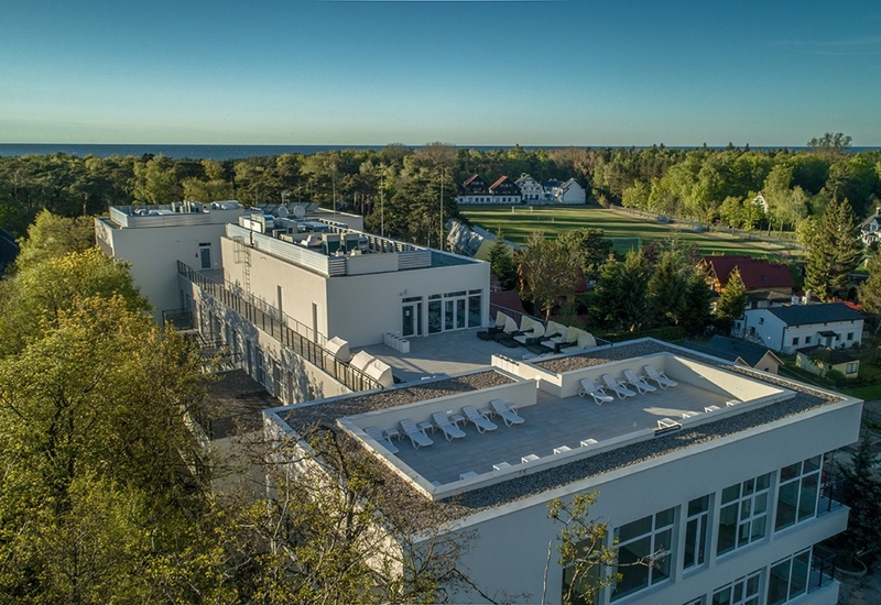 Nowoczesny hotel przy plaży z tarasem na dachu, leżakami i kabinami, widok na las i morze.