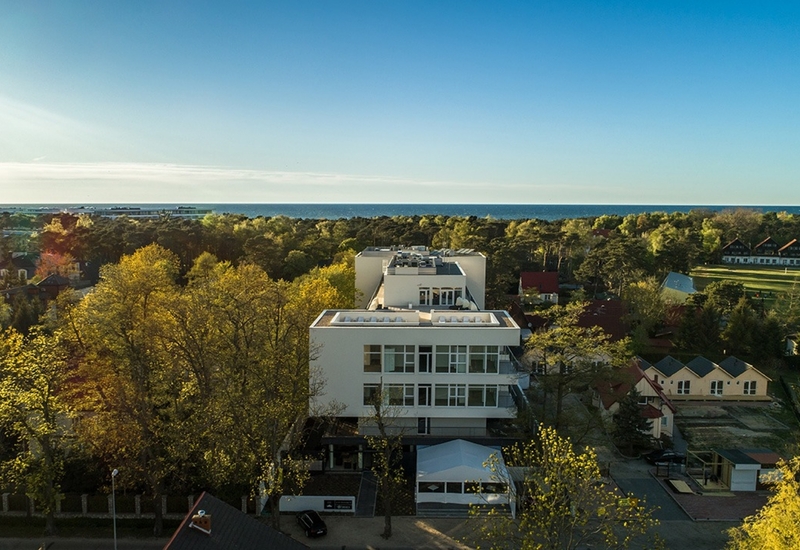 Nowoczesny, biały hotel z tarasami na dachu pośród sosnowego lasu, słoneczne tereny i widok na odległe morze