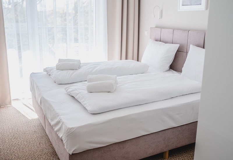 Jasny pokój hotelowy z dwoma łóżkami, białą pościelą, miękkim zagłówkiem, zwiniętymi ręcznikami i lekkimi zasłonami