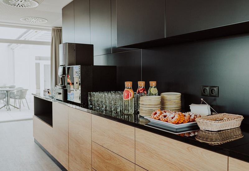 Nowoczesny bufet hotelowy z ekspresem do kawy, szkłem, karafkami wody z owocami, talerzami i ciastkami.