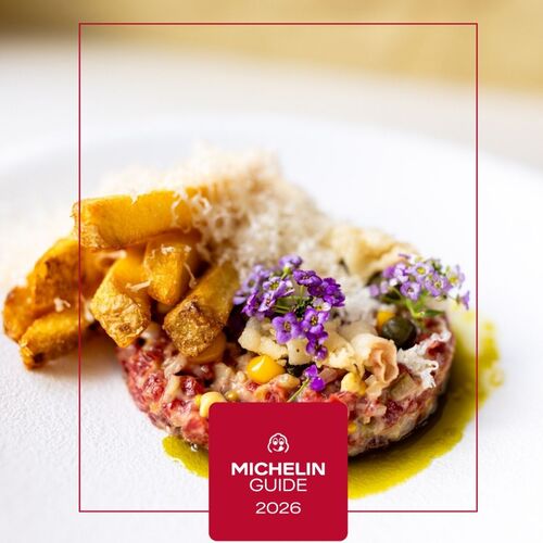 Tatar wołowy z chrupiącymi frytkami, startym serem, kukurydzą i jadalnymi fioletowymi kwiatami na zielonej oliwie, odznaka Michelin Guide 2026.