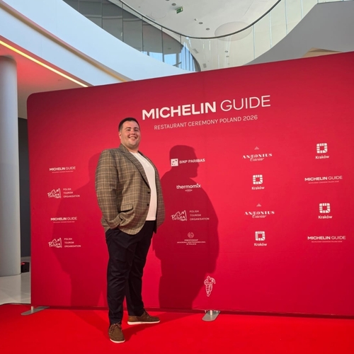 Gość pozujący na czerwonym dywanie podczas gali Michelin Guide Polska 2026, nowoczesne atrium z przeszklonym, zakrzywionym balkonem
