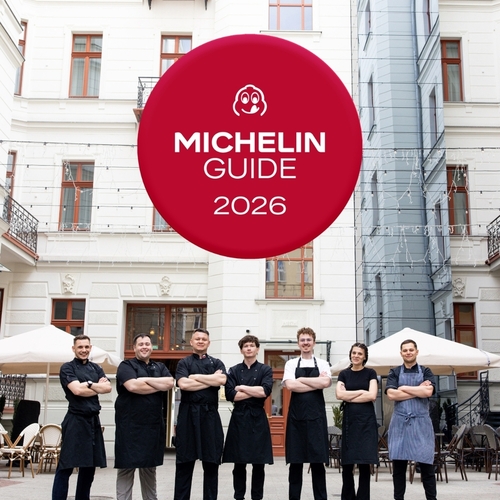 Zespół restauracji w czarnych fartuchach stoi na zabytkowym dziedzińcu hotelu z tarasem i czerwonym emblematem 'MICHELIN GUIDE 2026' nad głową.
