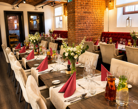 Gemütliches Restaurant mit gewölbter Backsteindecke, dunklen Holztischen, cremefarbenen Sesseln, roten Servietten, Blumen und Karaffen.