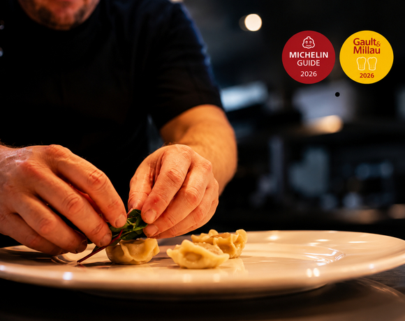 Ręce szefa kuchni układają ręcznie robione pierożki z mikroliśćmi na białym talerzu w restauracji nagrodzonej Michelin i Gault&Millau 2026.