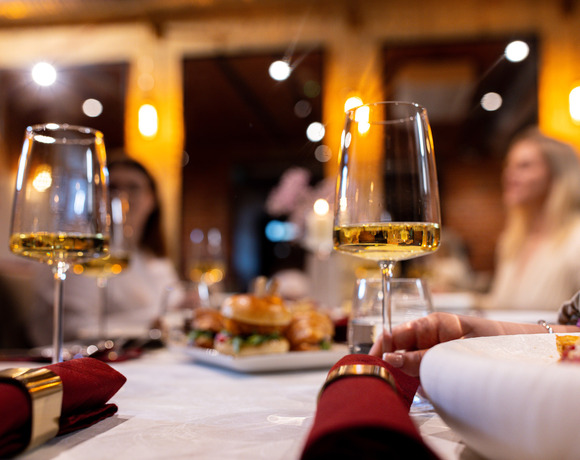 Przytulny stół w restauracji z kieliszkami białego wina, bordowymi serwetkami, przystawkami i rozmytymi gośćmi