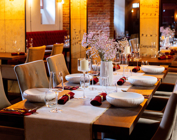 Elegancka restauracyjna zastawa na kolację, miękkie pikowane krzesła, świece, kieliszki i różowy bukiet gipsówki, ceglana ściana.