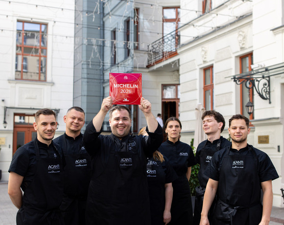 Zespół restauracji w czarnych fartuchach w zabytkowym dziedzińcu, szef kuchni trzyma czerwony znak 'MICHELIN 2026', radosna atmosfera