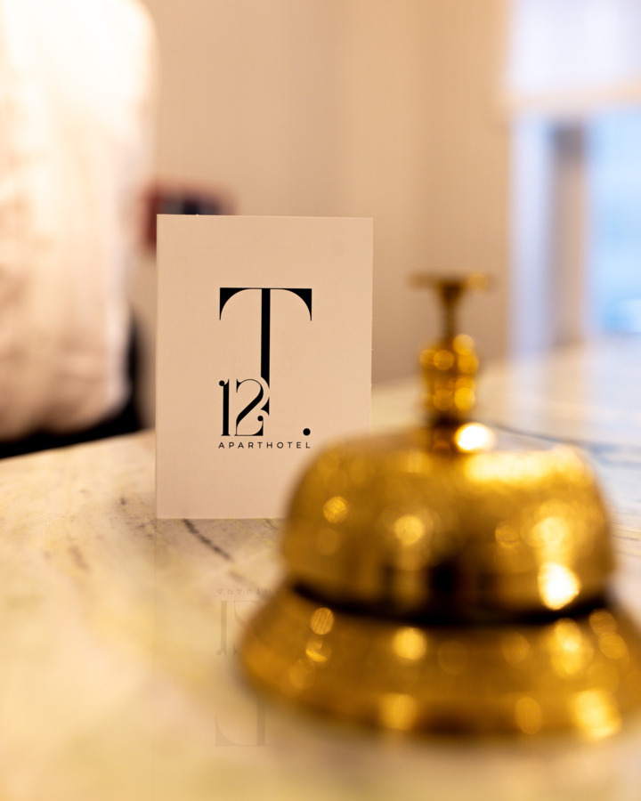 Złoty dzwonek recepcyjny na marmurowym blacie obok eleganckiej karty z logo apart-hotel T12