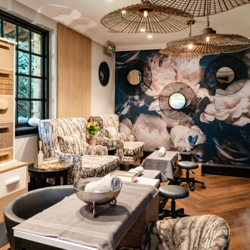 Hotel spa pedicure room with plush armchairs, footbaths and stools, nail polish wall, floral mural and woven pendant lights