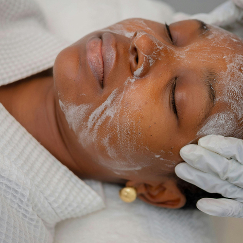 Guest receiving a relaxing facial at hotel spa with cleansing mask, gloved esthetician hand and white waffle spa robe.