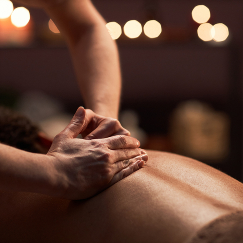 Therapist's hands giving a relaxing back massage in a candlelit spa treatment room with warm, ambient lighting.