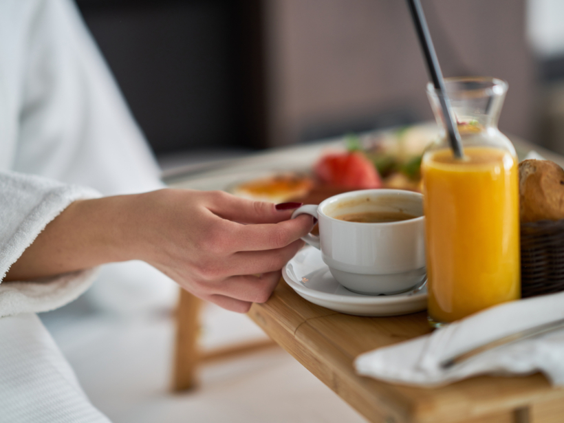 Kobieta delektująca się śniadaniem oraz napojami dostarczonymi do pokoju zamówionego room servicu