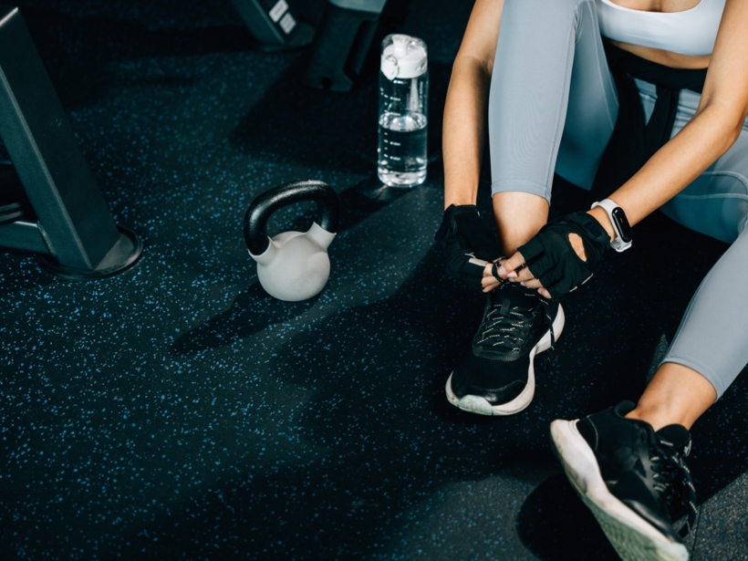 Kobieta wiążąca buty przed treningiem w strefie fitness, obok woda i hantel
