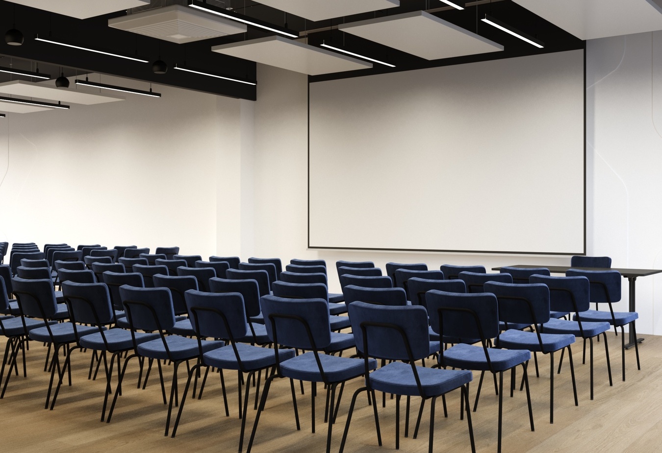 Sala konferencyjna z rzędami granatowych krzeseł, dużym ekranem projekcyjnym, nowoczesnym oświetleniem sufitowym i drewnianą podłogą.