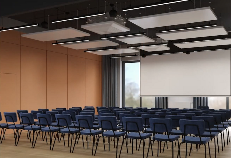 Sala konferencyjna z rzędami niebieskich krzeseł, dużym ekranem, drewnianą podłogą i nowoczesnymi panelami sufitowymi.