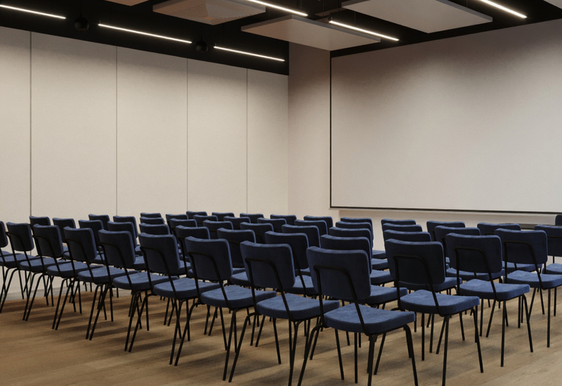 Sala konferencyjna z rzędami niebieskich krzeseł, dużym ekranem projekcyjnym, drewnianą podłogą i nowoczesnym oświetleniem.