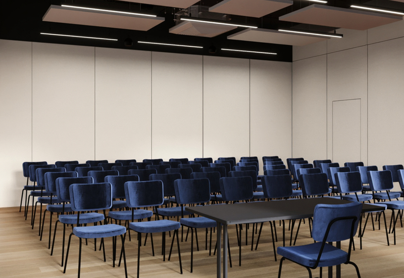 Sala konferencyjna z rzędami granatowych krzeseł, stołem prelegenta, drewnianą podłogą i akustycznym sufitem.