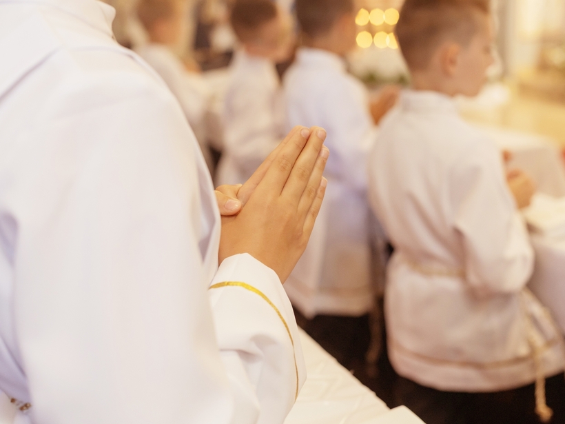 Chłopcy w białych albach z złożonymi dłońmi do modlitwy podczas ceremonii w kościele, ciepłe światło świec w tle
