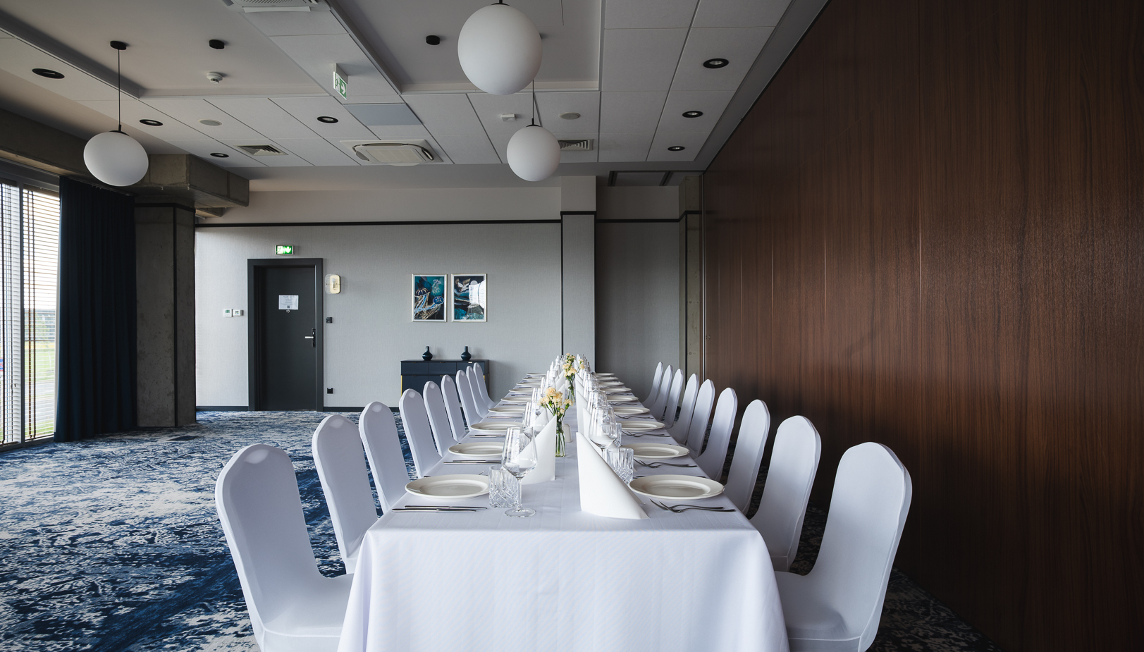 Elegancka sala konferencyjna z długim stołem nakrytym białym obrusem, ustawiona na bankiet z białymi krzesłami i dekoracjami