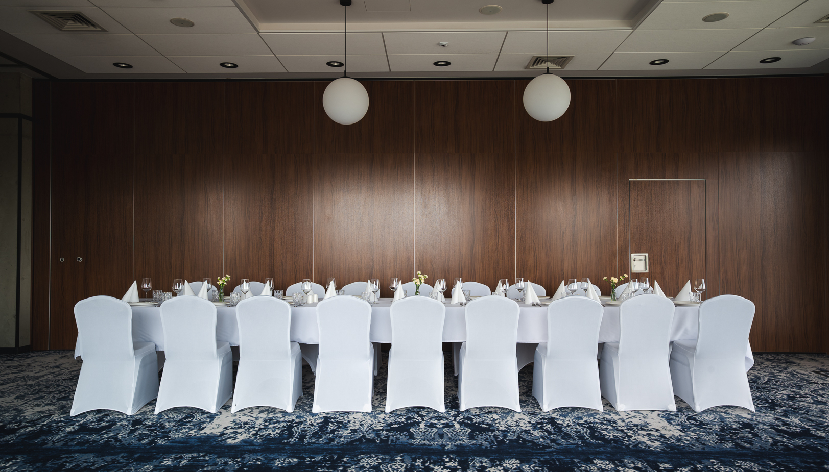 Elegancki stół bankietowy z białymi pokrowcami na krzesłach, finezyjnym nakryciem i kwiatowymi dekoracjami w sali konferencyjnej.