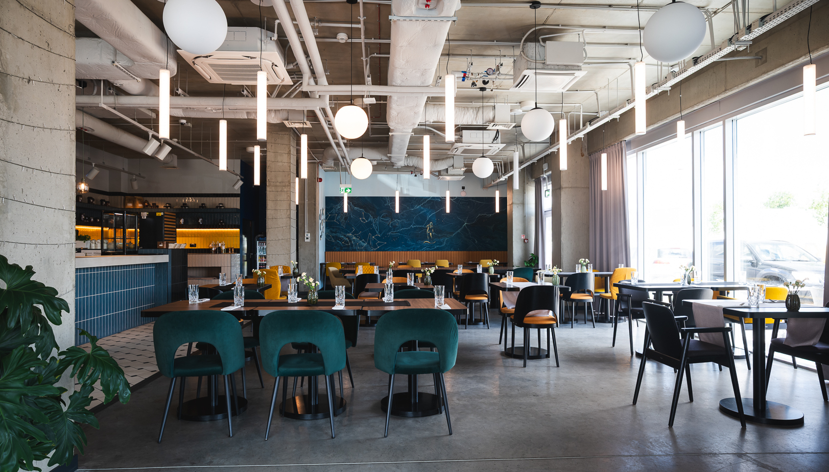 Nowoczesna restauracja z komfortowymi zielonymi i żółtymi krzesłami, designerskim oświetleniem i dużymi oknami z naturalnym światłem.