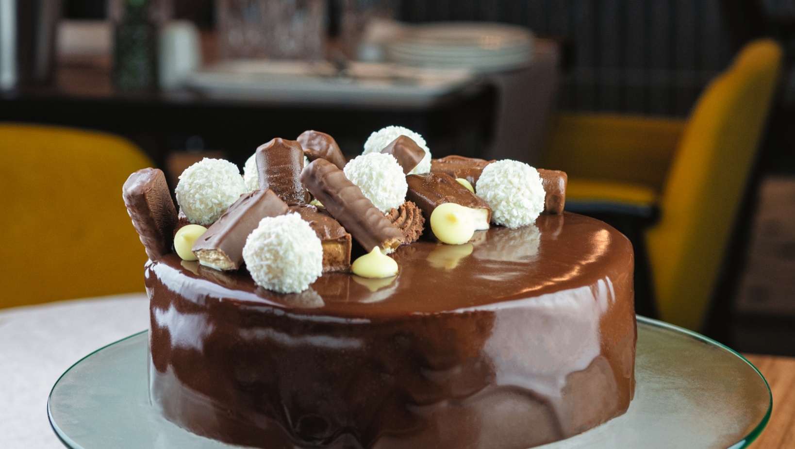 Lśniące czekoladowe ciasto z dekoracją z pralinek i białych kokosowych kulek, na szklanym talerzu w restauracji