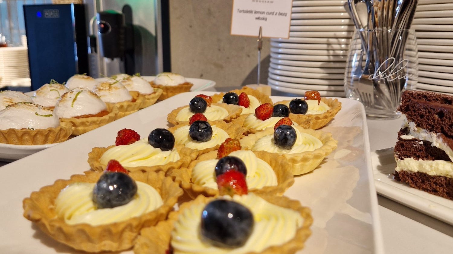 Wybór słodkich tartaletek z kremem i owocami oraz kawałek wilgotnego ciasta czekoladowego na bufecie hotelowym.