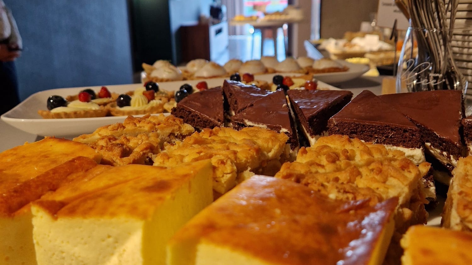 Zestaw różnorodnych deserów: sernik, ciasto czekoladowe i owoce na kremowych tartaletkach.