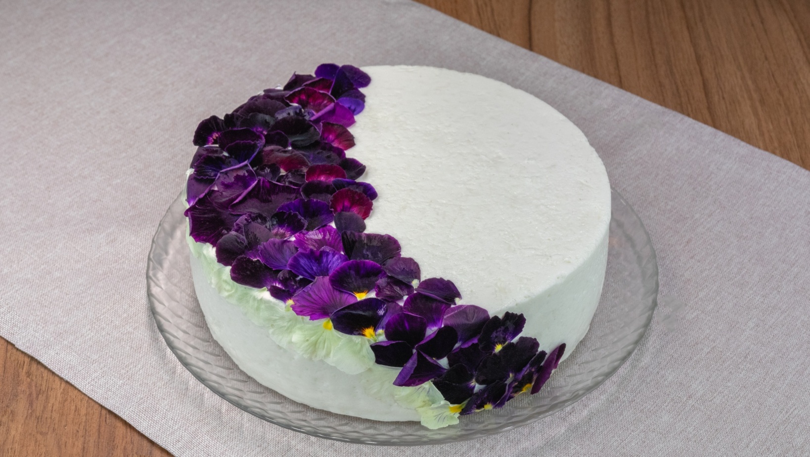 Eleganckie białe ciasto ozdobione połową świeżych, fioletowych kwiatów na przezroczystym talerzu