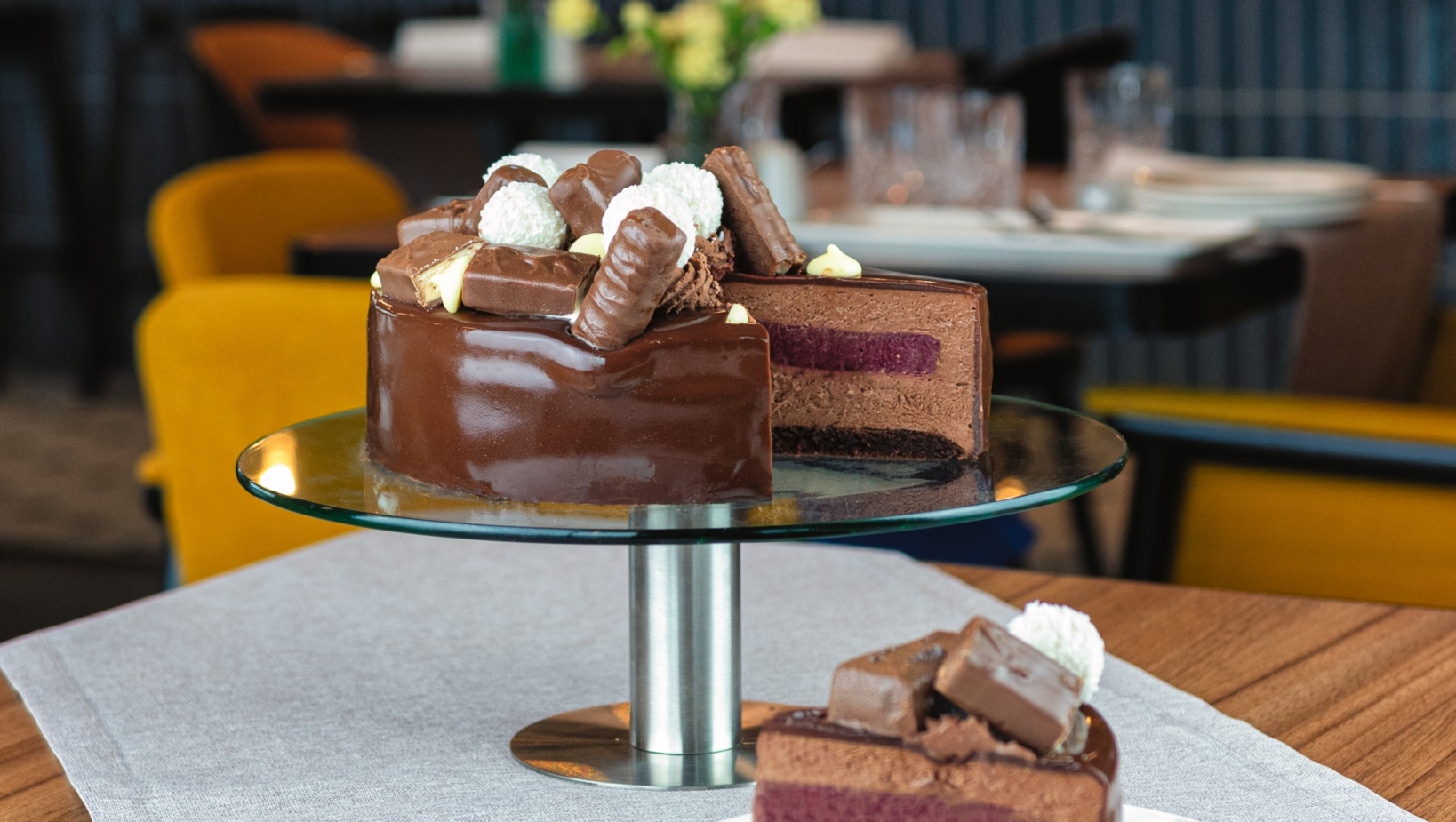 Czekoladowe ciasto na szklanym stojaku w eleganckiej restauracji, ozdobione pralinkami i kulkami kokosowymi