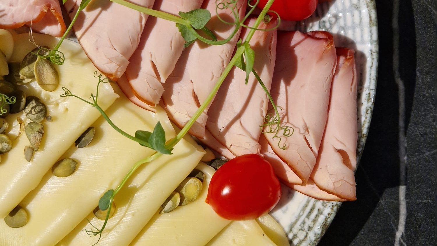 Plastry szynki i sera ozdobione pestkami dyni i świeżym zielonym pędem na eleganckim talerzu