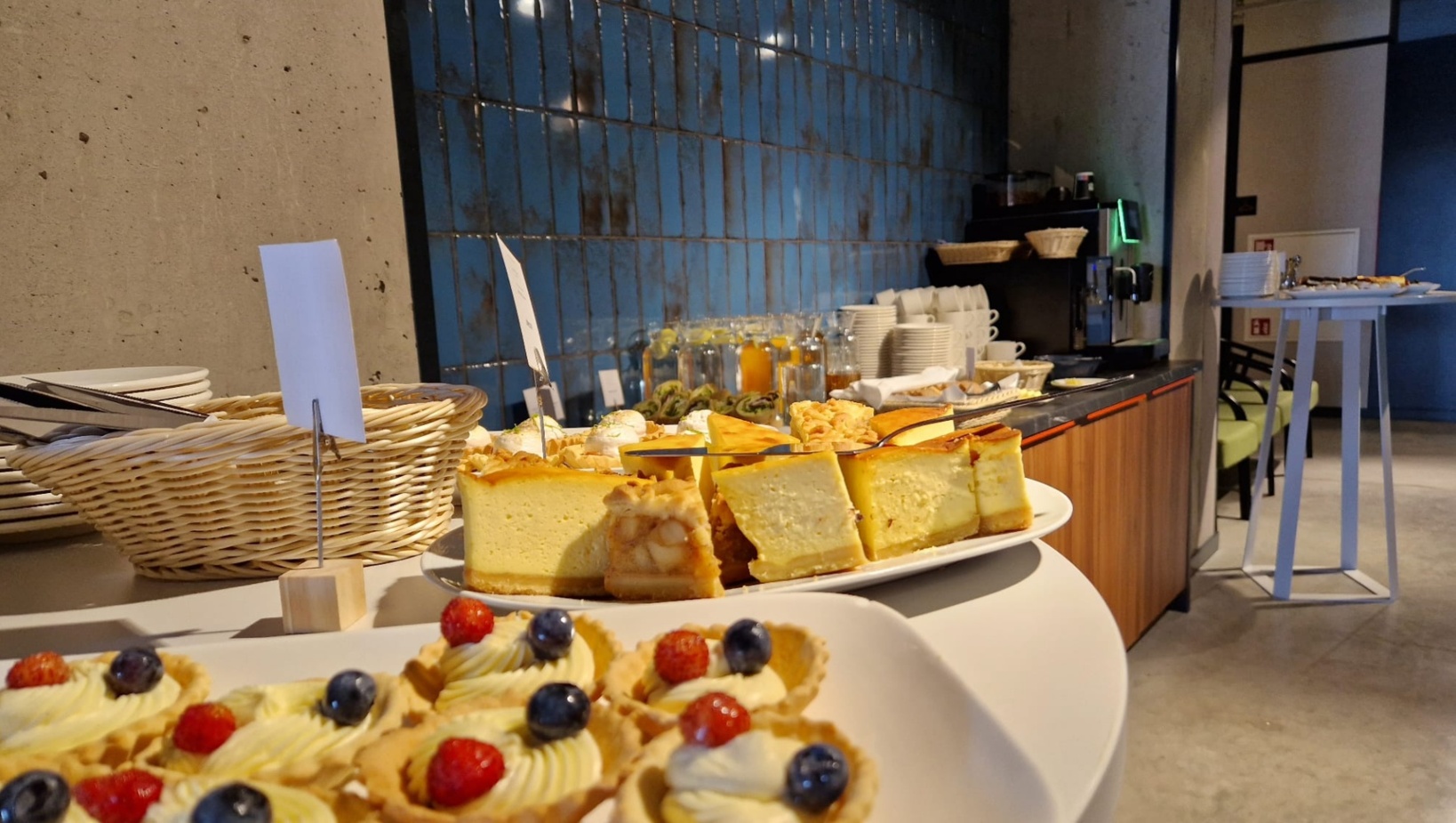 Bufet hotelowy z różnorodnymi deserami, serwowanym ciastem, tartaletkami z owocami oraz zestawem filiżanek i soków.